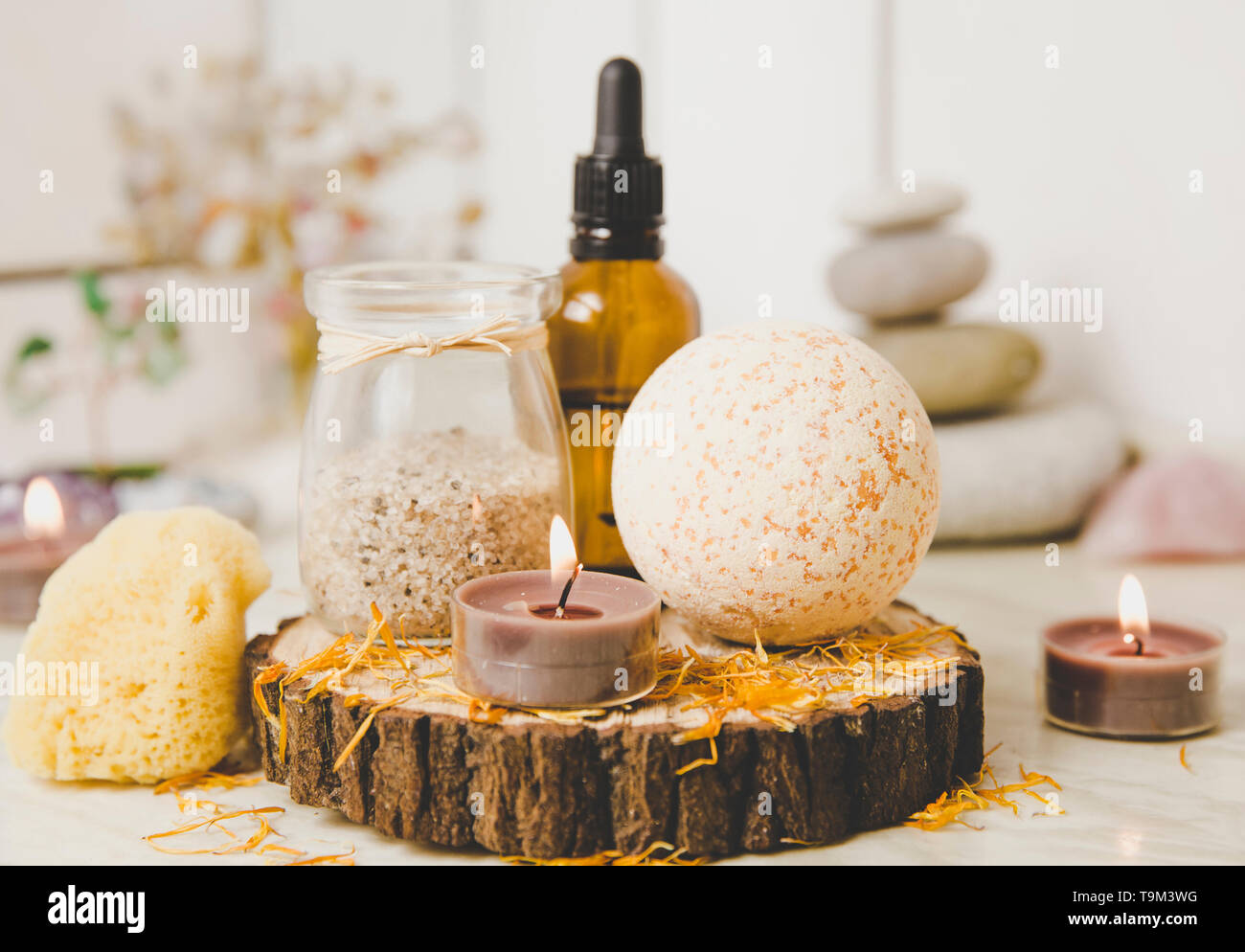 Vista laterale di home wellness spa prodotti bagno arancione bomba, bagno aromatico sale, spugna del mare, tè candele accese. Molto zen impostare, albero di amore e ametista cryst Foto Stock