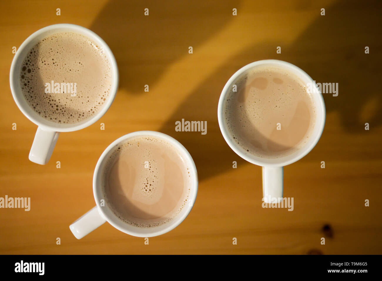 Tre bianchi tazza di latte caldo, caffè o cacao su un tavolo di legno, vista dall'alto, primo piano Foto Stock