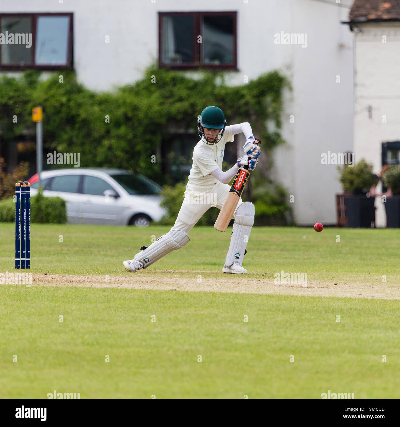 Cricket su un villaggio verde nel Kent. Regno Unito. Un battitore colpisce un coperchio rigido per il boundry Foto Stock