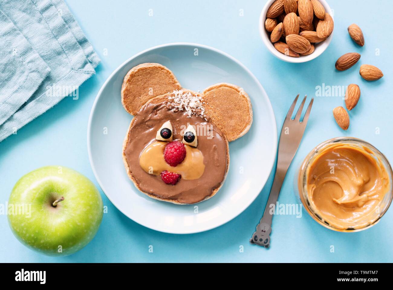 Il cibo della colazione per i bambini. A forma di animale pancake con dado di cioccolato burro e frutti, sfondo blu Foto Stock