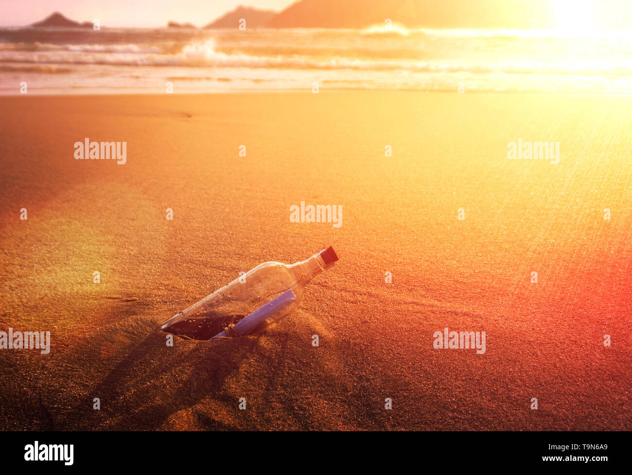 Messaggio in una bottiglia di vetro tappati sulla spiaggia dell'oceano al tramonto dorato concettuale Foto Stock