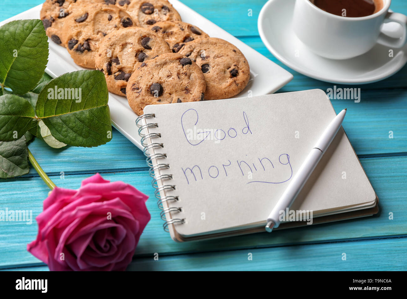 Piastra con gustosi biscotti al cioccolato, una tazza di caffè e di buon mattino nota in notebook sul colore tavolo in legno Foto Stock