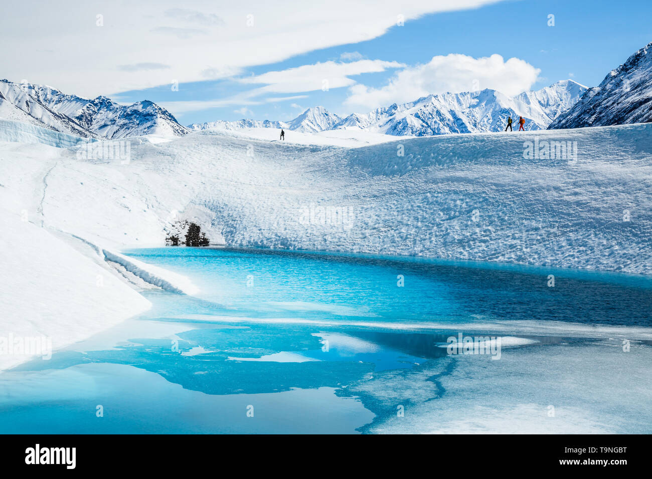 Te scalatori trekking attraverso il ghiacciaio Matanuska oltre un profondo lago blu sulla parte superiore del ghiacciaio in Chugach Mountains. Foto Stock