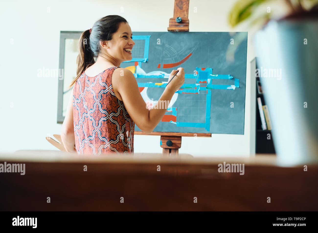 Ritratto di ispanici giovane donna dipinto nel suo studio di casa, esercitando con vernice, pennello, cavalletto e colore per hobby. Foto Stock