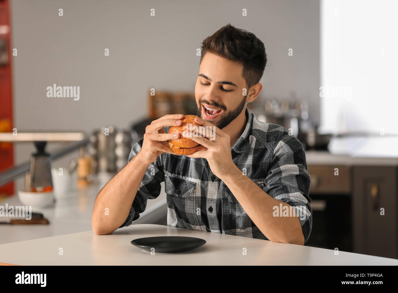 Giovane uomo mangiare saporito burger a casa Foto Stock