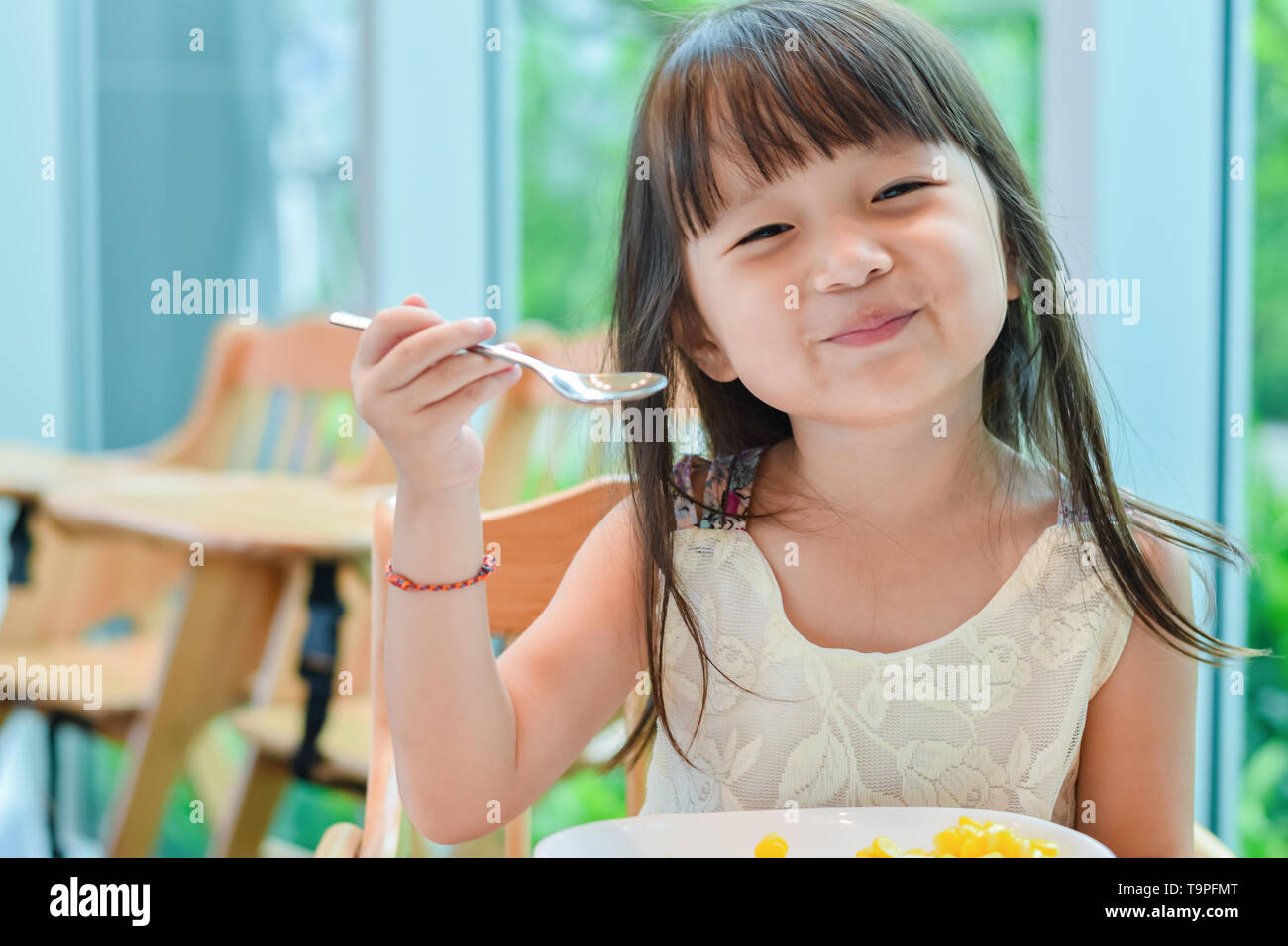 Piccolo bambino asiatico ragazza avente la prima colazione al mattino con un felice volto sorridente Foto Stock