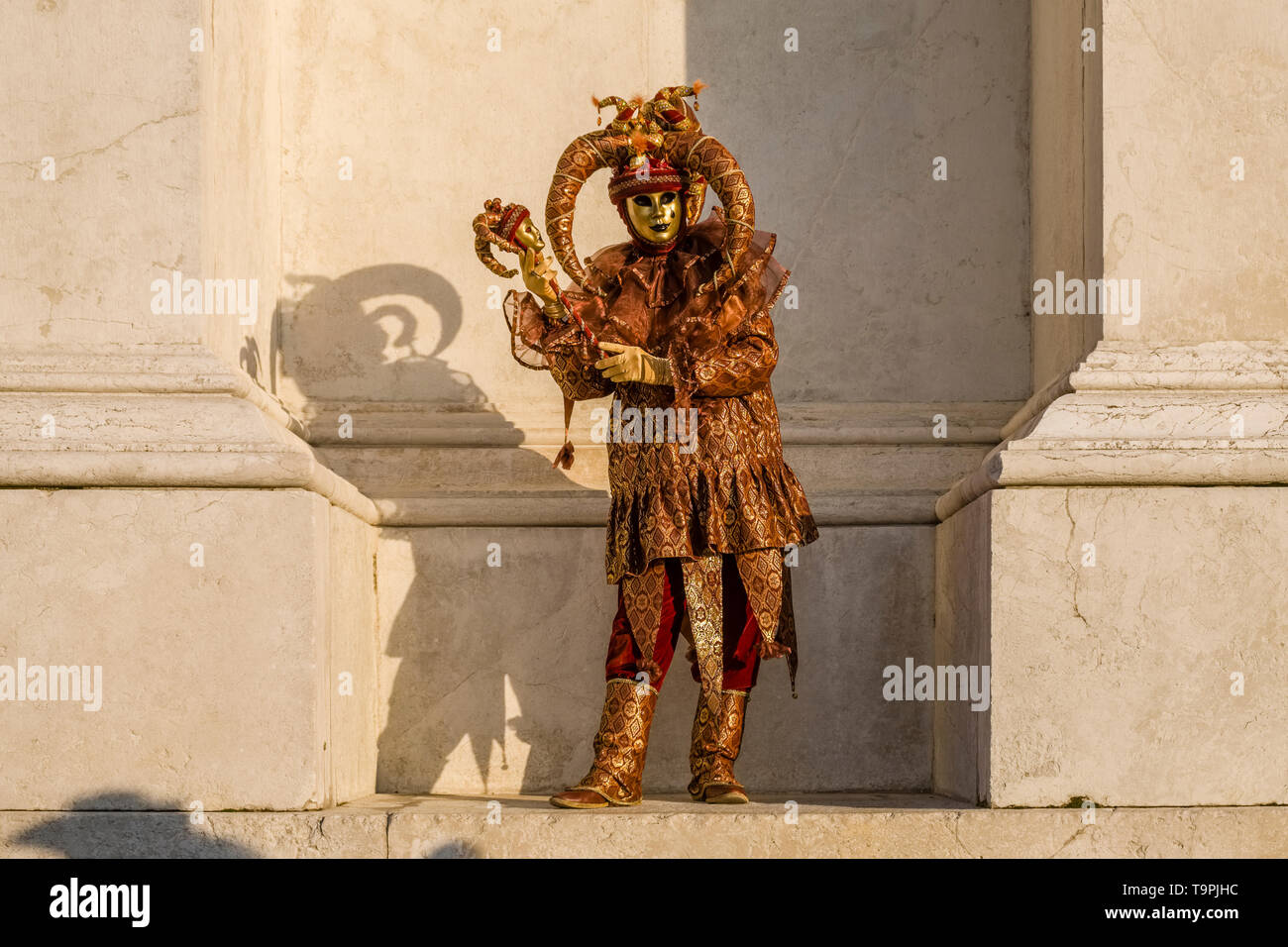 Un masculin persona mascherato in una bella creative costume di Arlecchino, posa sull'isola di San Giorgio di Maggiore, celebra il Carnevale Veneziano Foto Stock