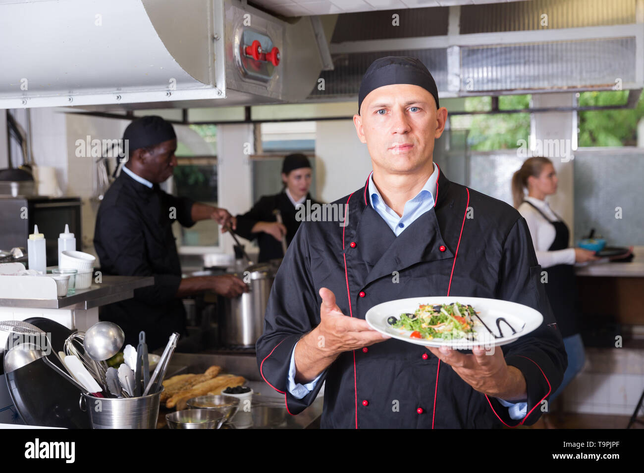 Professionale chef del ristorante moderno tenendo piatto finito, pronto a servire agli ospiti Foto Stock