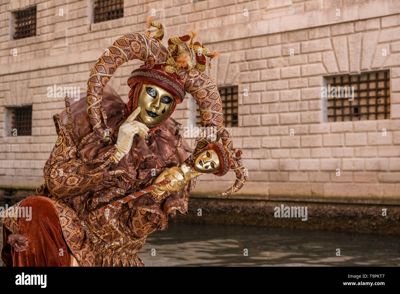 Ritratto di un masculin persona mascherato in una bella creative costume di Arlecchino, ponendo sotto i portici di Palazzo Ducale, Palazzo Ducale Foto Stock