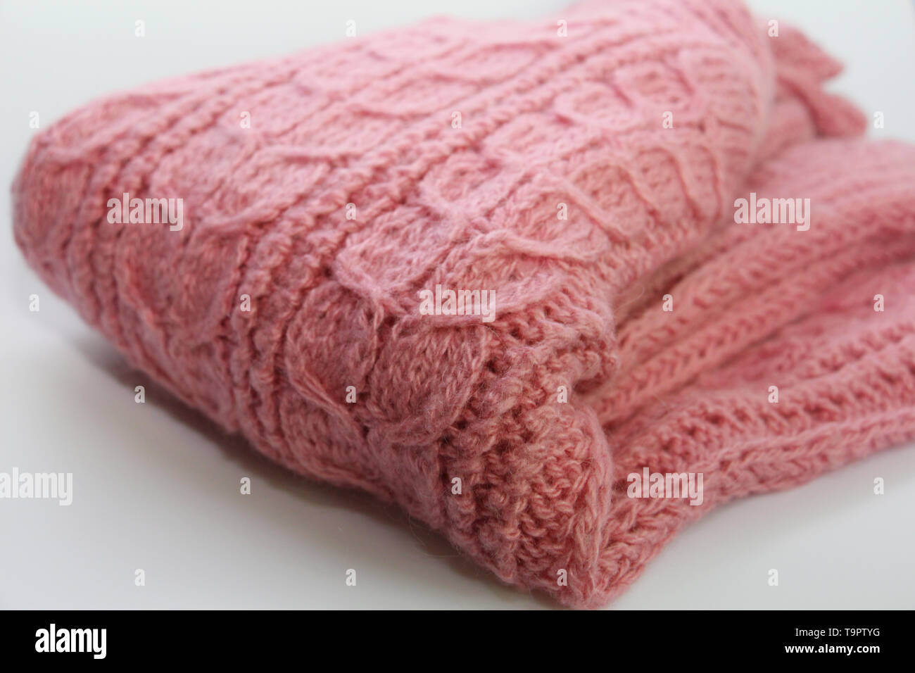 Un caldo colore rosa felpa lavorata a maglia è sdraiato su uno sfondo bianco. Un bel disegno è visibile su il maglione. Modello unico di close-up. Maglione è complic Foto Stock