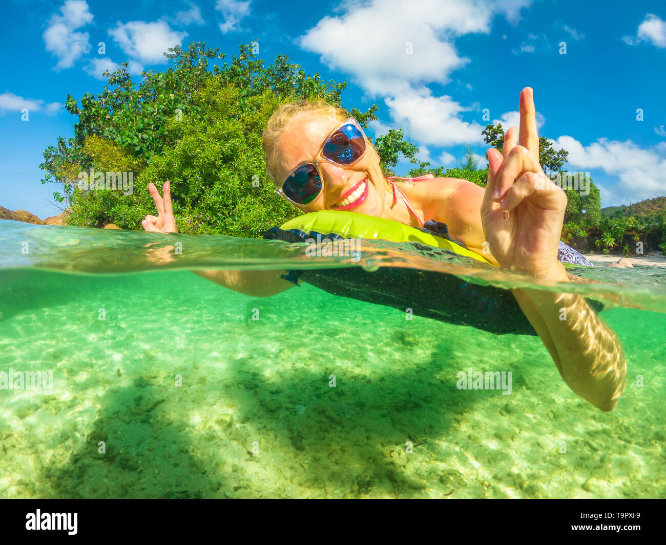 La vista suddivisa di donna a prendere il sole e rilassarsi sul materasso con parte subacquea nel mare di Anse Takamaka, Praslin, Seychelles, Oceano Indiano. Estate Foto Stock