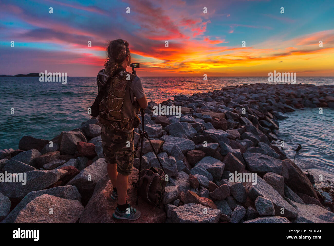 Fotografo di viaggio con il treppiede su rocce frangiflutti ad Anse Kerlan, Seicelle con scenic colorato sky. Spiaggia di Kerlan, a sud-ovest di Praslin è famosa per Foto Stock