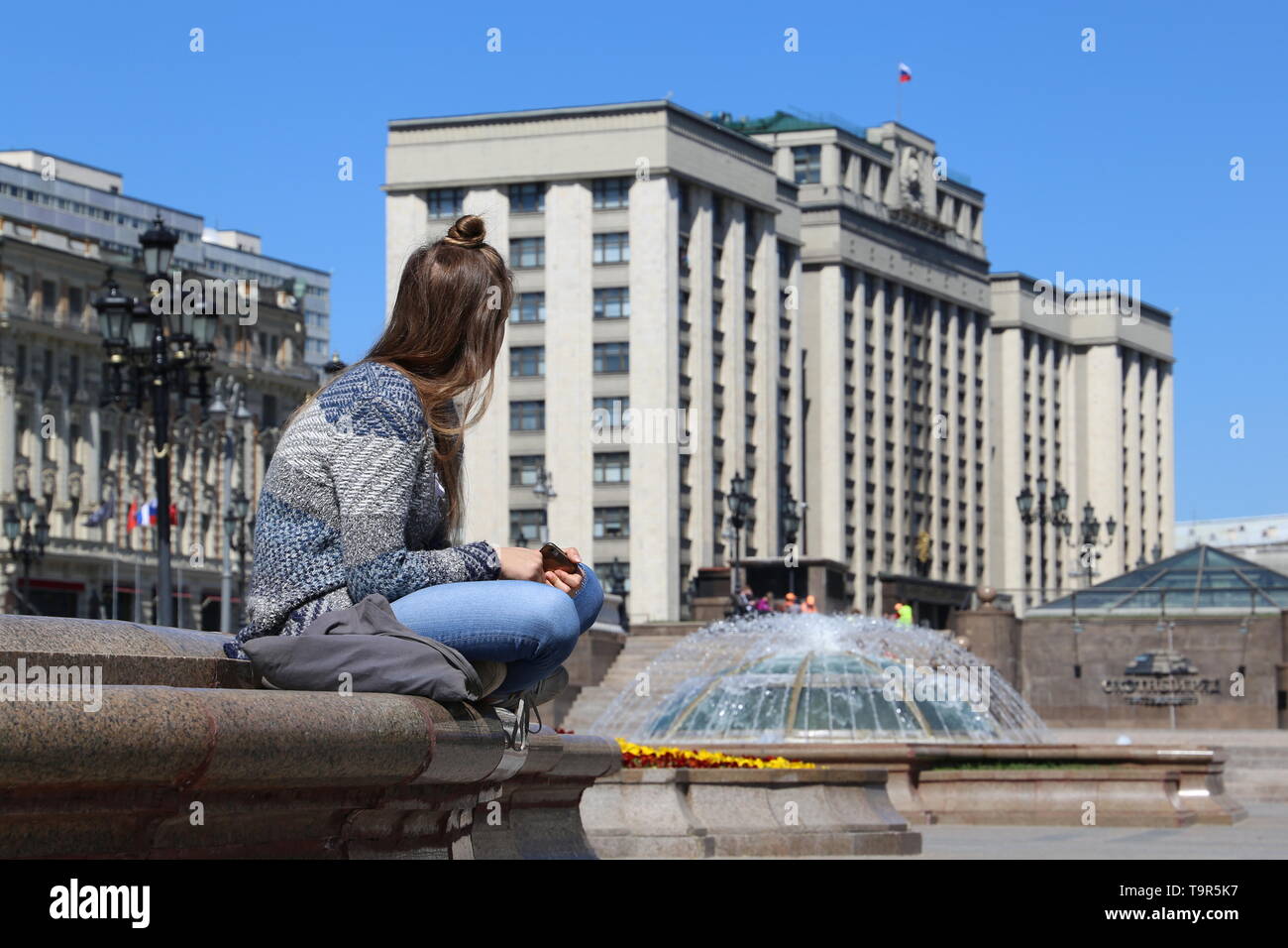 Ragazza seduta con lo smartphone sul background del parlamento russo edificio e fontana a Mosca. Vista sulla città in tempo soleggiato, il concetto di turismo, Foto Stock