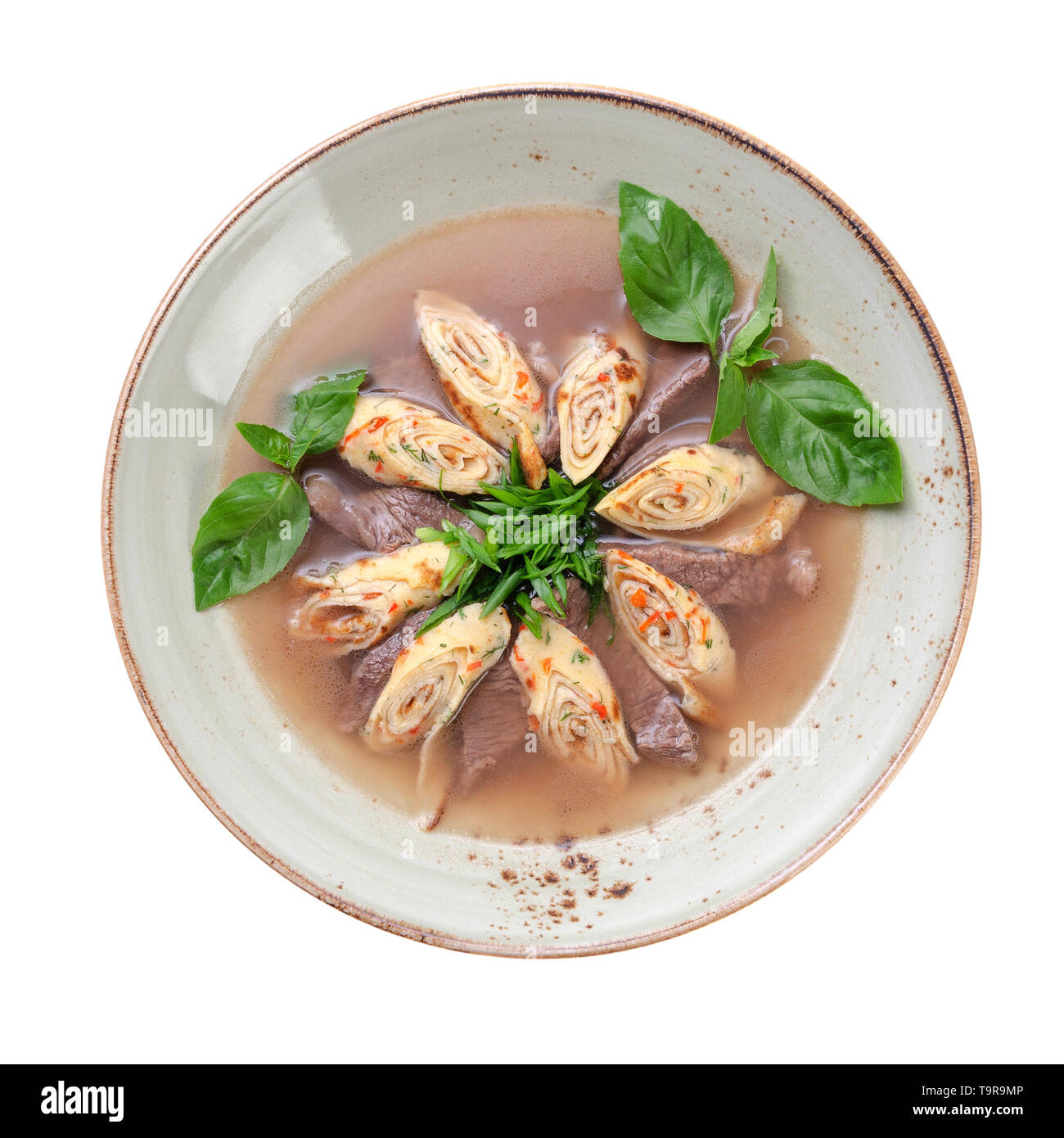 Zuppa con fette di carne di manzo, e pancake arrotolato in forma di rotolo, decorata con verdi. isolato su sfondo bianco Foto Stock