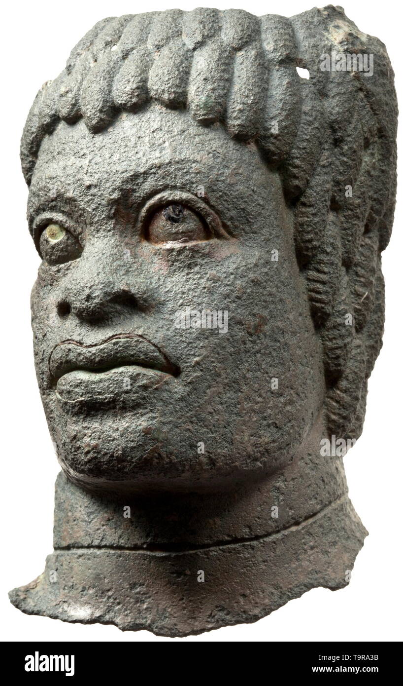 Una testa romana di un Africano maschio con funzioni di negroid, 2° - 3° secolo frammento di un bronzo balsamarium. Completamente preservato la faccia di un uomo nero con vetro intarsiato di allievi. Anche il rame intarsi in corrispondenza dei bordi delle labbra. Intorno al collo una scanalatura che ha tenuto il materiale ad inserti per il ruolo di una collana. Ampia naso e grandi labbra. Grossolanamente capelli modellato. Sulla parte superiore sinistra di un a palmette, sul quale l'anello della maniglia mancante è stato saldato. Superficie leggermente corroso. Bene anche oliva-patina verde. Altezza 10,5 cm. Lo stile eccellente di alta qualità con distintivi po, Additional-Rights-Clearance-Info-Not-Available Foto Stock