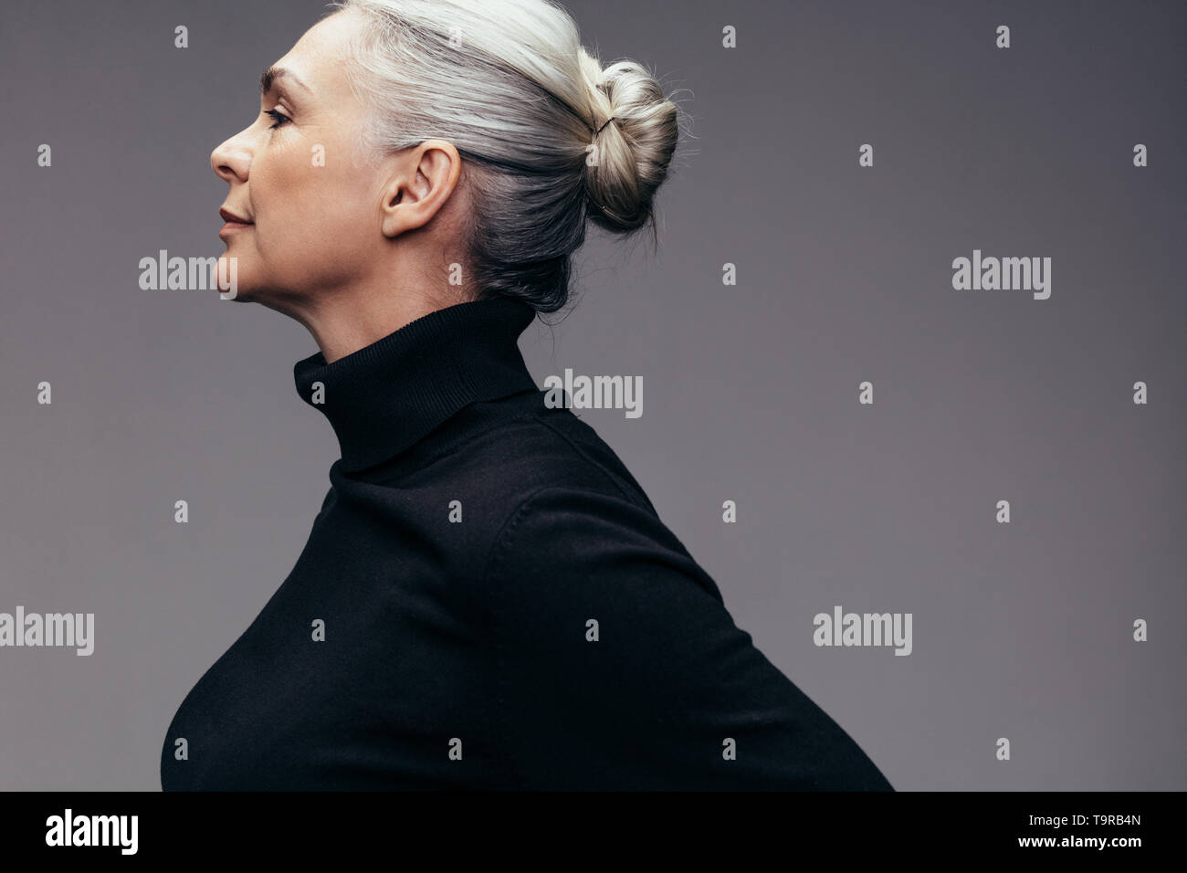 Vista di Profilo di donna matura in casuals nero su sfondo grigio. Senior caucasian donna con capelli bun. Foto Stock
