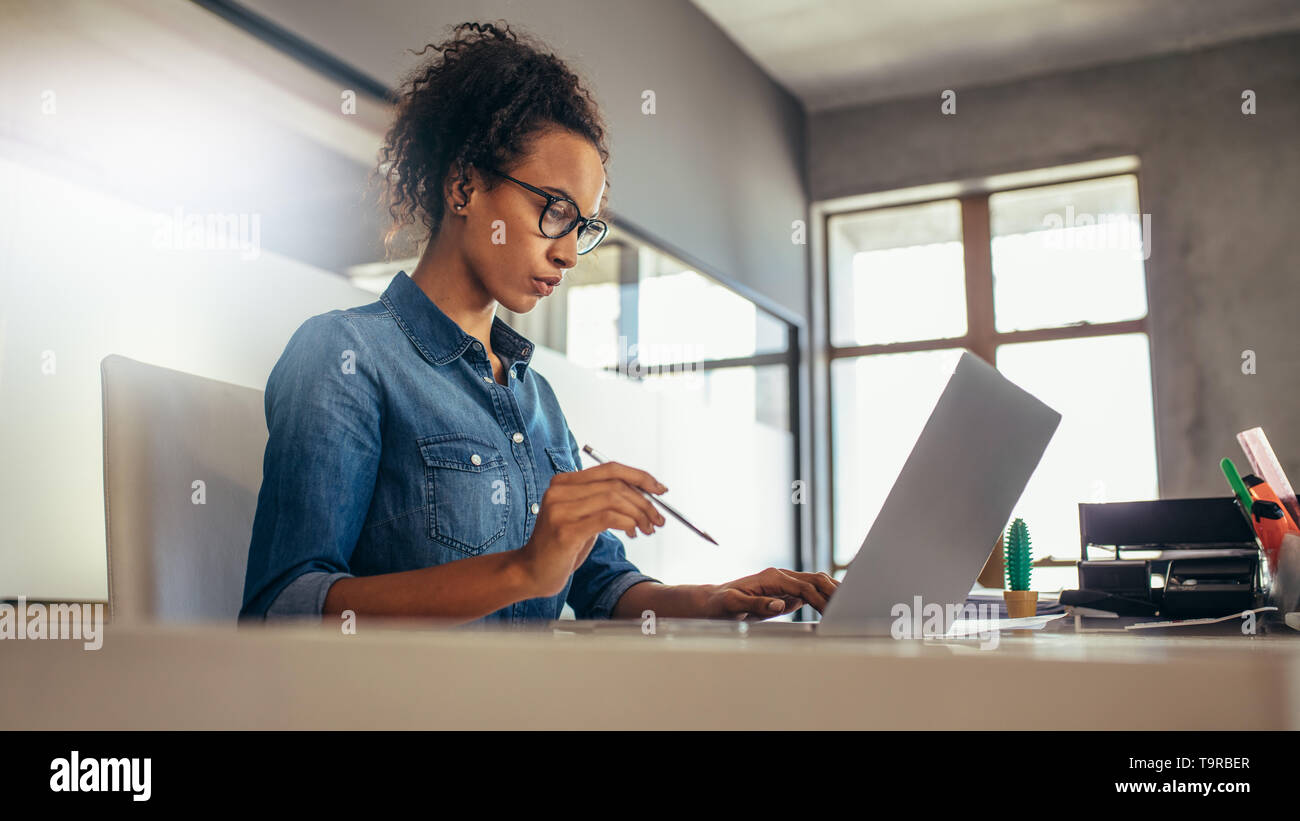 Giovane imprenditrice lavorando alla sua scrivania. Lavoro femminile sul computer portatile in ufficio. Foto Stock
