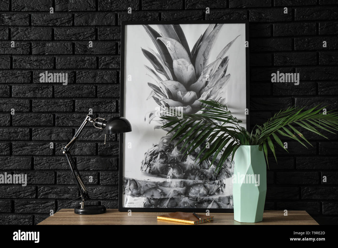 Vaso con foglie tropicali, immagine e la lampada sul tavolo vicino a scuro muro di mattoni Foto Stock