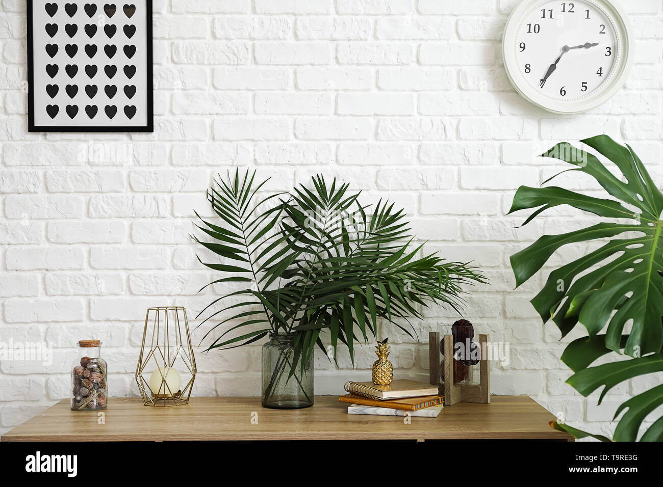Vaso con verde tropicale, lascia sul tavolo vicino a parete di luce Foto Stock