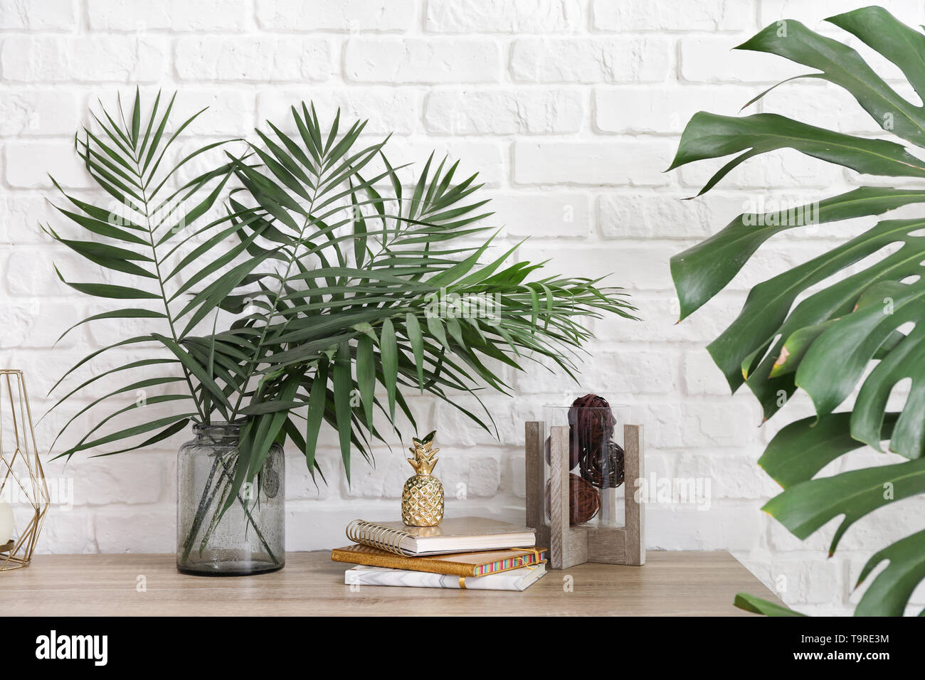 Vaso con verde tropicale, lascia sul tavolo vicino a parete di luce Foto Stock