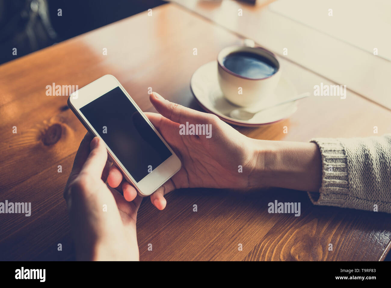 Donna che utilizza smartphone sul tavolo di legno al cafe'. Close-up immagine con reti sociali di concetto Foto Stock