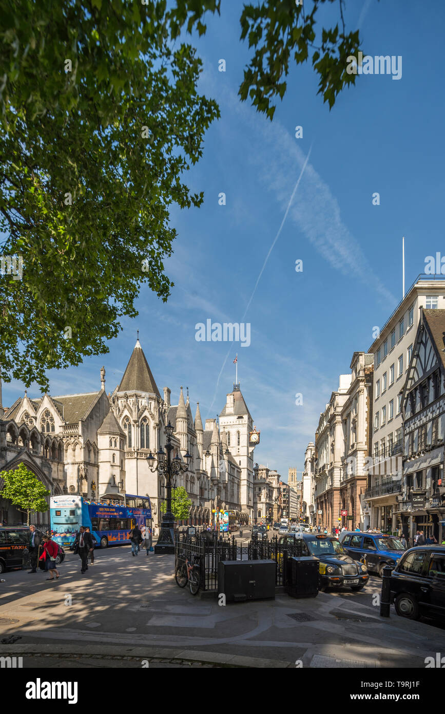 Una vista di Strand nel centro di Londra con i Royal Courts of Justice sulla sinistra e alberi frondosi appesi sopra in una giornata di sole estati Foto Stock