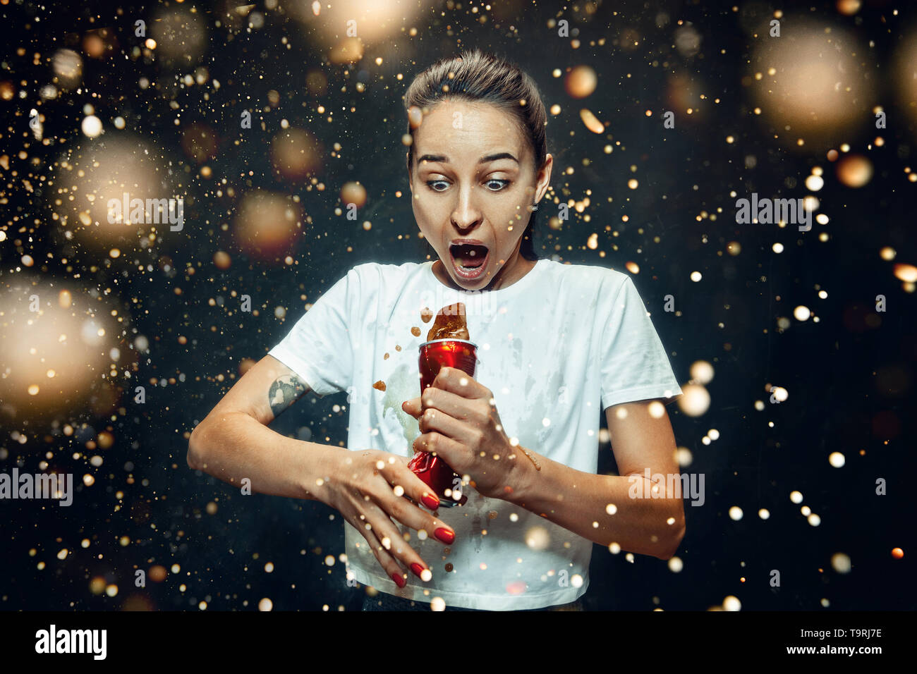 Donna di bere una coca cola in studio. Giovani felici sorridente ragazza caucasica apertura può con cola e godendo di spruzzo. L'immagine pubblicitaria circa drink preferito. Lo stile di vita e le emozioni umane concetto. Foto Stock