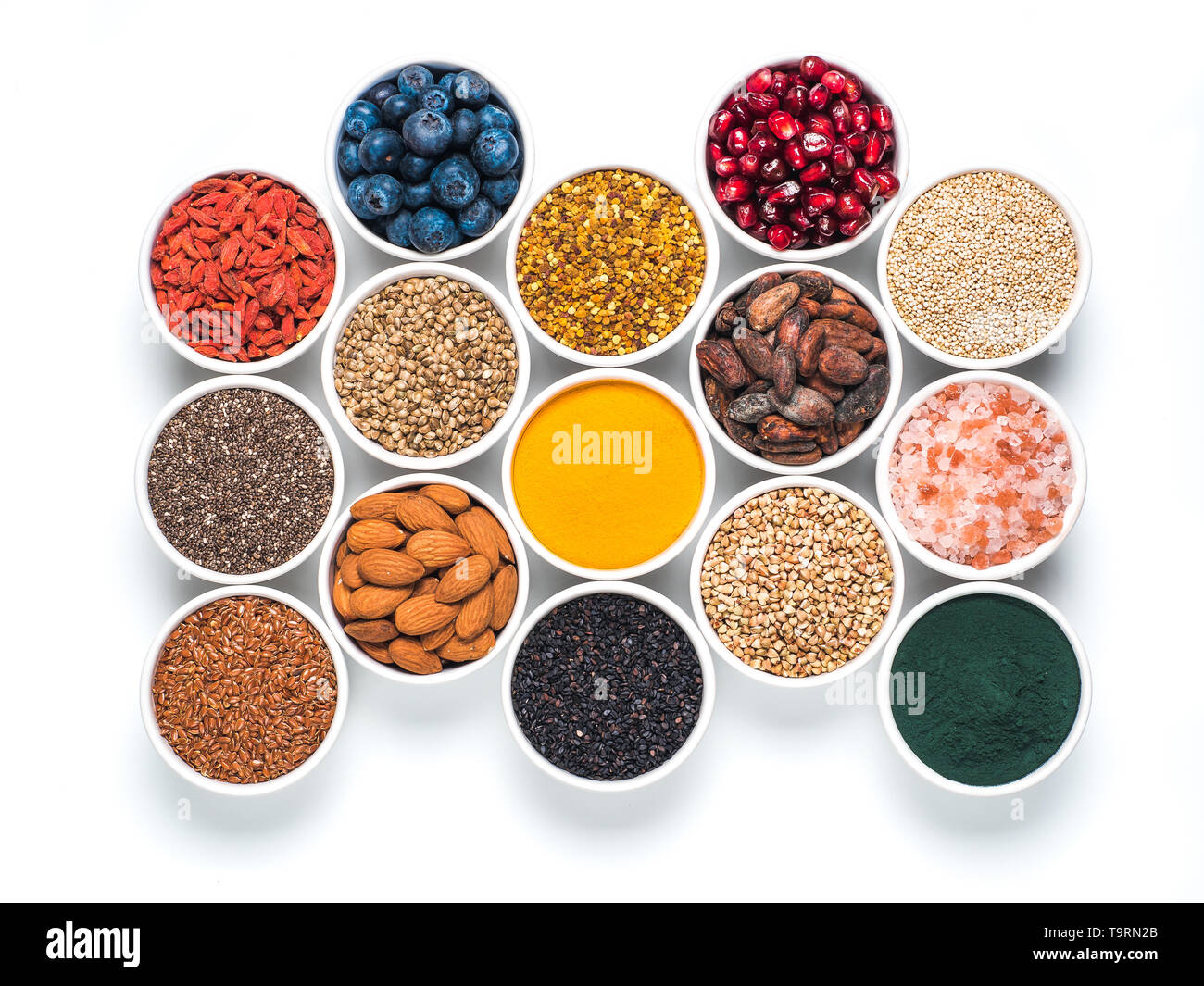 Varie superfoods nel piccolo recipiente isolato su sfondo bianco. Super come chia, spirulina, materie fava di cacao, goji, canapa, quinoa, polline di api, sesamo nero, curcuma. Vista superiore o flat-lay. Foto Stock