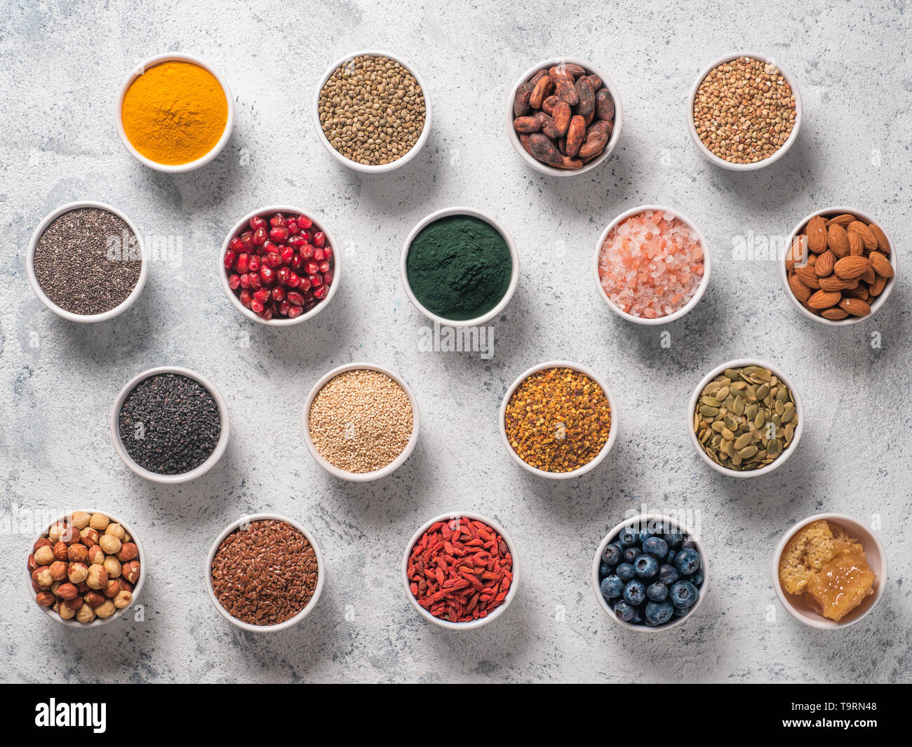 Varie superfoods nella piccola ciotola di cemento grigio Sfondo. Super come chia, spirulina, materie fava di cacao, goji, canapa, quinoa, polline di api, sesamo nero, curcuma. Vista superiore o flat-lay. Foto Stock