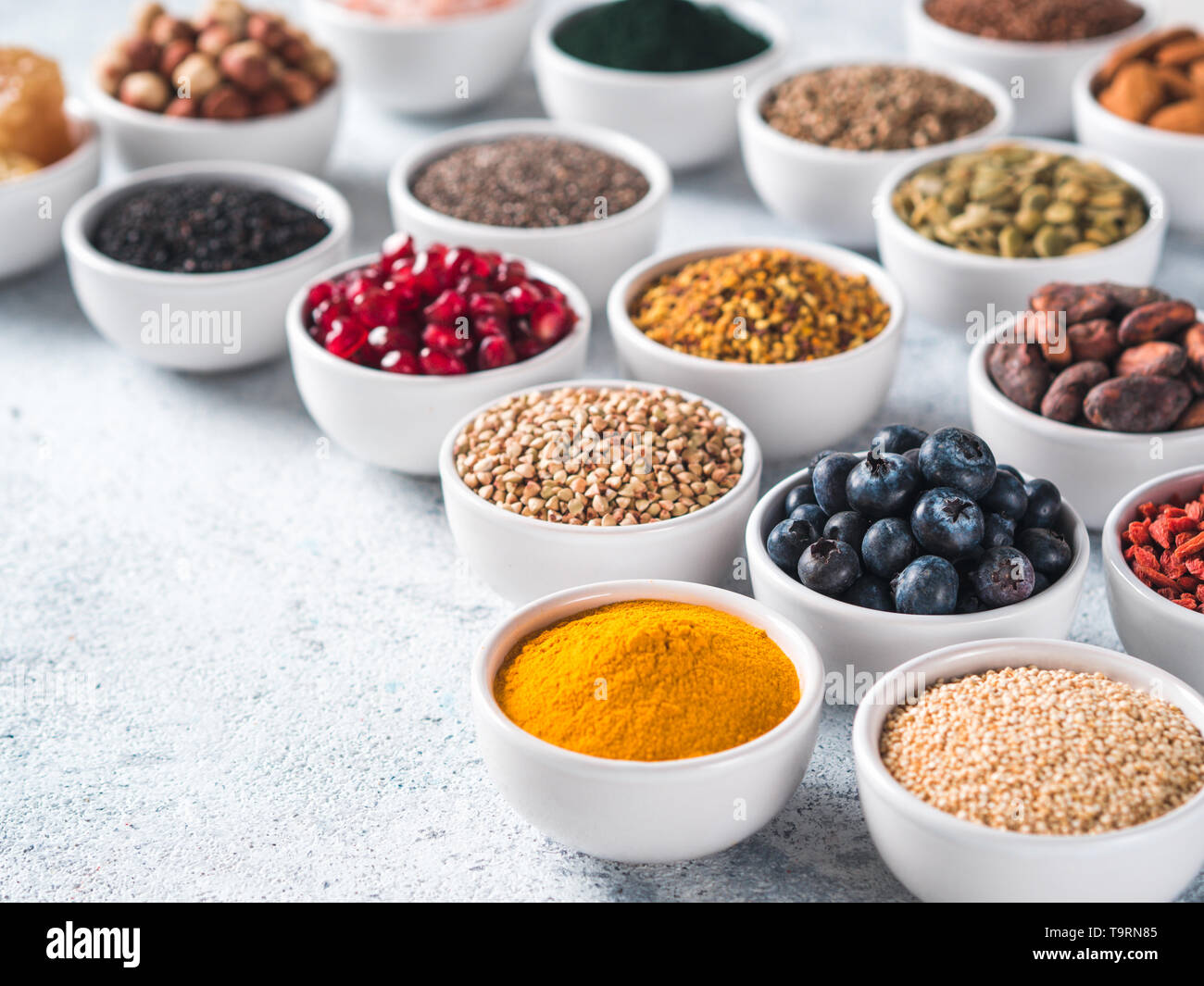 Varie superfoods nella piccola ciotola di cemento grigio Sfondo. Super come chia, spirulina, materie fava di cacao, goji, canapa, quinoa, polline di api, sesamo nero, curcuma. Copia spazio per il testo. Foto Stock