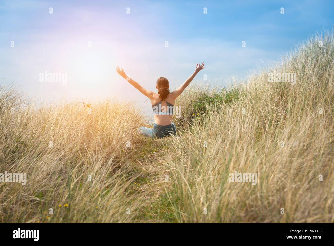 Sportivo da donna seduta nella posizione del loto con le braccia sollevate al cielo la meditazione. BCK vista. Foto Stock