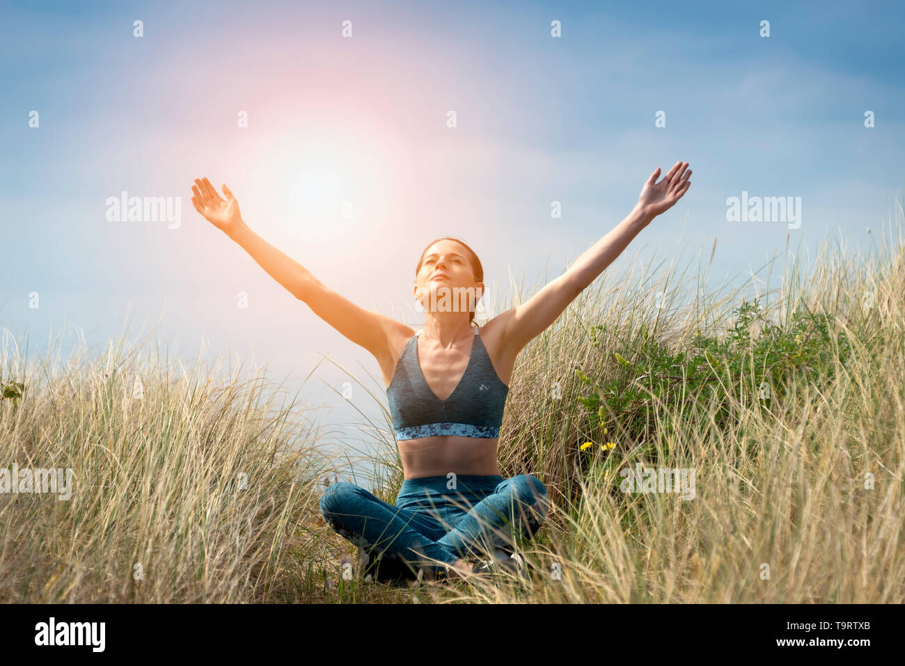 Sportivo da donna seduta nella posizione del loto con le braccia sollevate al cielo e gli occhi chiusi in meditazione. Foto Stock