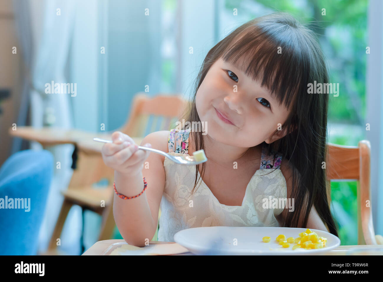 Piccolo bambino asiatico ragazza avente la prima colazione al mattino con un felice volto sorridente e mostrando il cibo su un cucchiaio Foto Stock