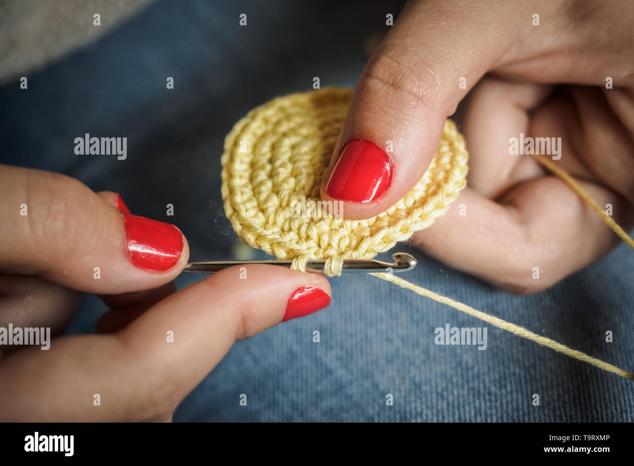 Ragazza crochet facendo con filo giallo e unghie dipinte di rosso, vicino a fotografare Foto Stock