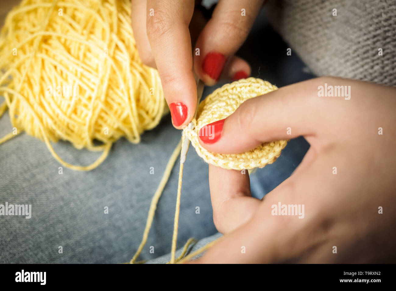 Ragazza crochet facendo con filo giallo e unghie dipinte di rosso, vicino a fotografare Foto Stock