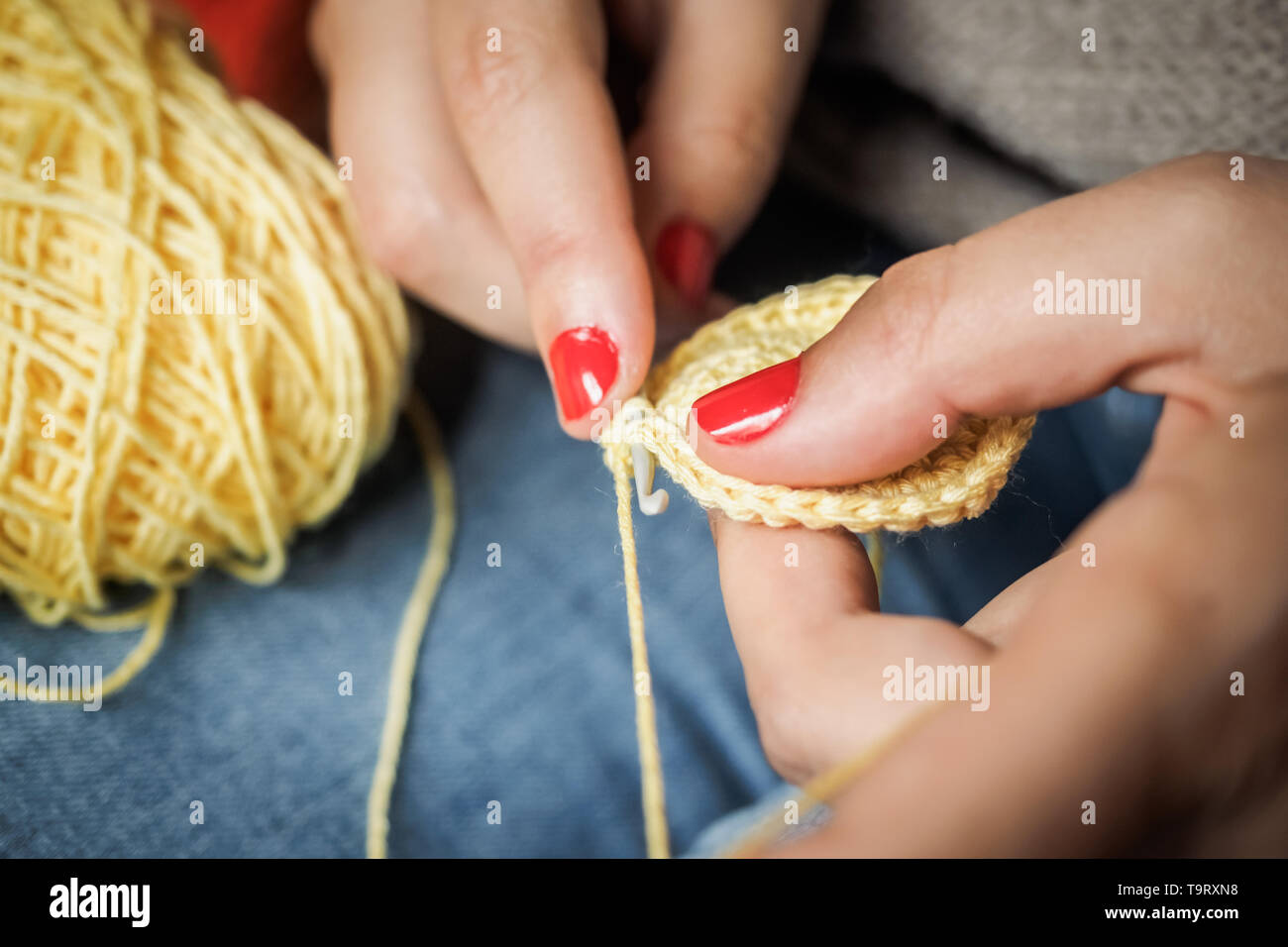 Ragazza crochet facendo con filo giallo e unghie dipinte di rosso, vicino a fotografare Foto Stock