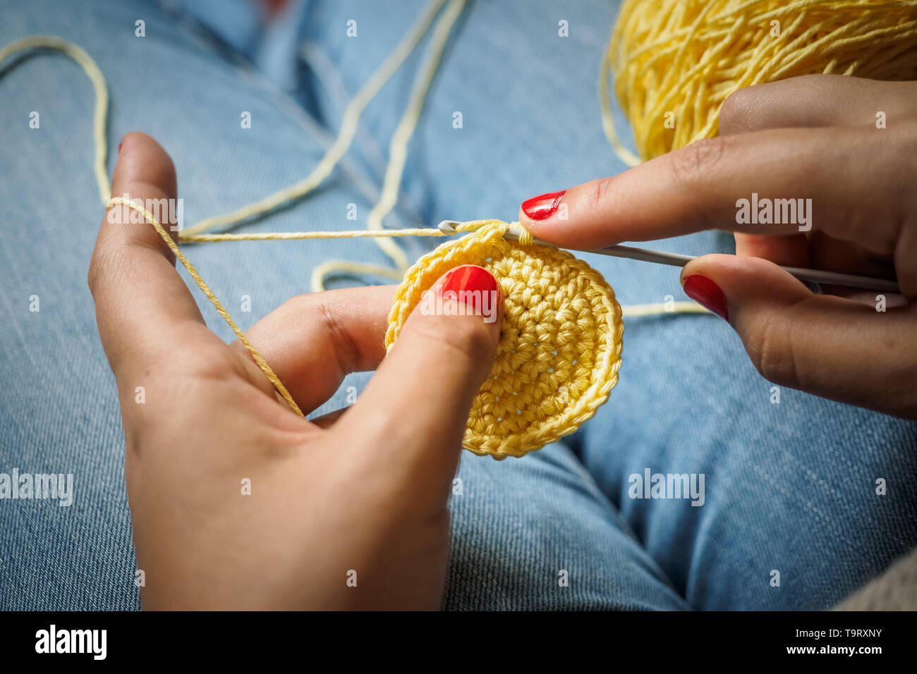 Ragazza crochet facendo con filo giallo e unghie dipinte di rosso, vicino a fotografare Foto Stock