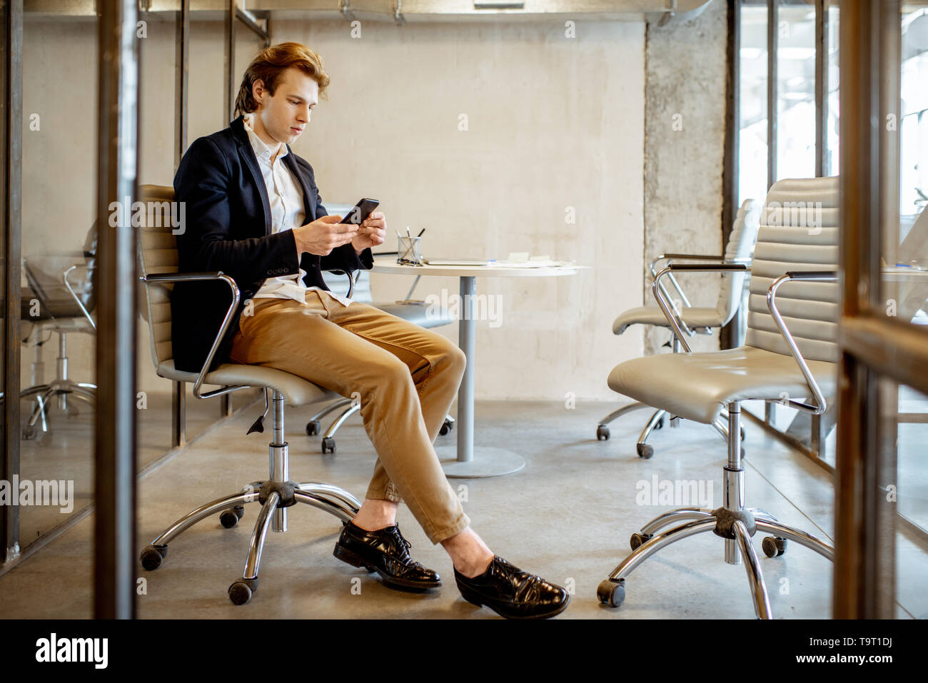 Giovane imprenditore seduta con lo smartphone durante la pausa caffè nella sala riunioni Foto Stock