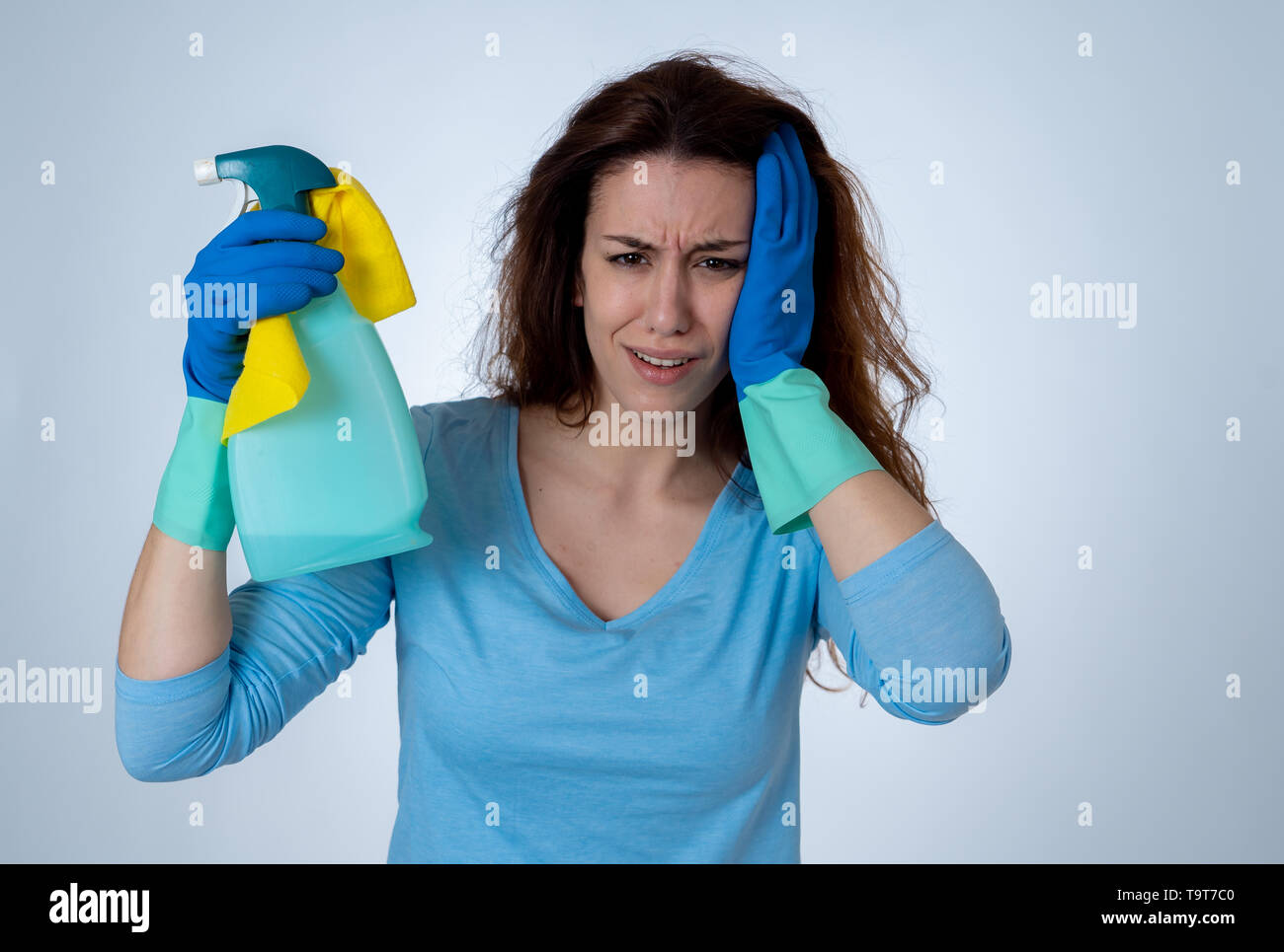Giovani belle sconvolto casalinga donna tenendo la benna mop spray per la pulizia di sensazione ha sottolineato stanco e deluso in compiti domestici e i ruoli di genere conc Foto Stock