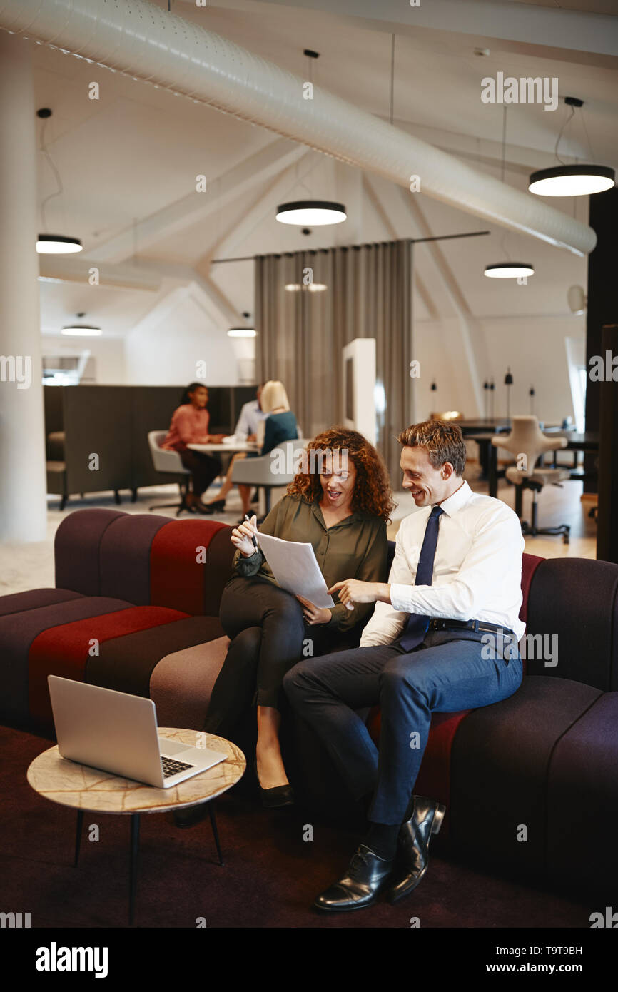 Due diversi colleghi per discutere insieme dei documenti mentre è seduto su un divano in un ufficio moderno Foto Stock