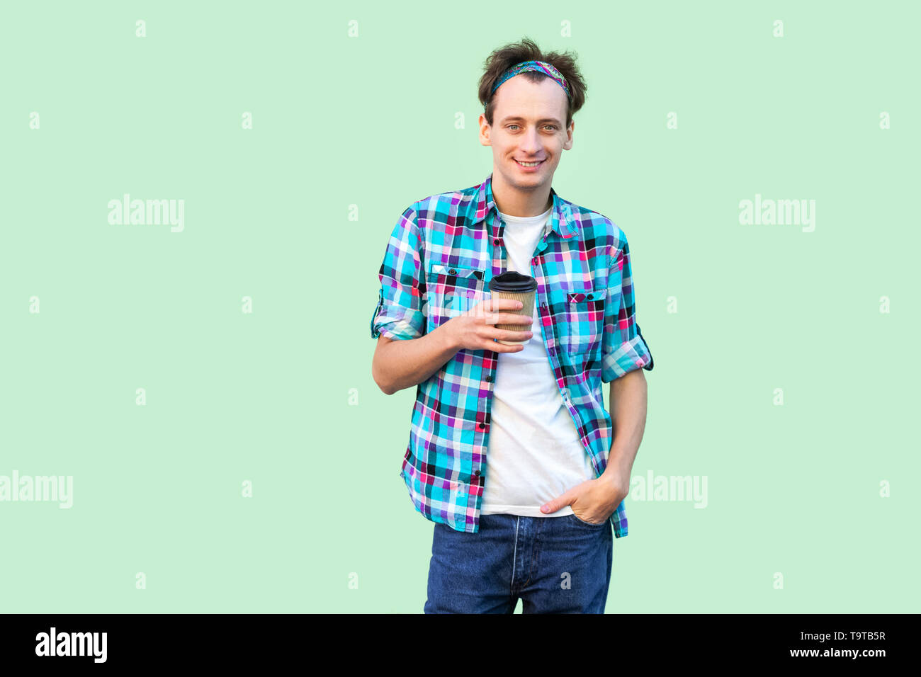 Prendere una pausa caffè. giovani hipster uomo in bianco t-shirt e camicia a scacchi in piedi tenendo la carta con la tazza di caffè al mattino con la mano in tasca. Piscina Foto Stock