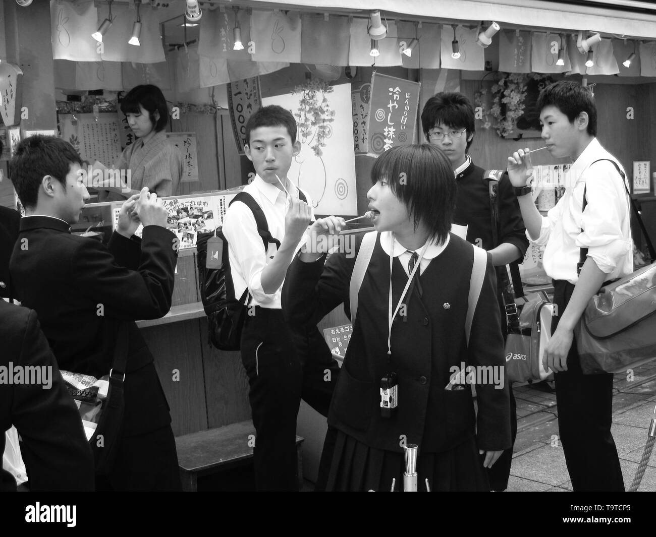 Giapponese scolari una sosta per uno spuntino in un alimento in stallo a Tokyo durante la fioritura dei ciliegi tempo Foto Stock