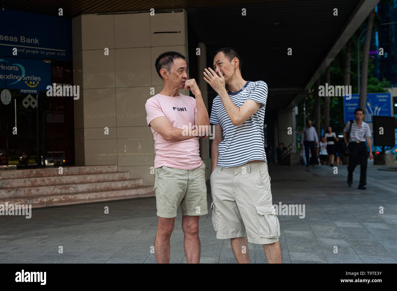 09.05.2019, Singapore, Repubblica di Singapore, in Asia - due uomini sono in chat in quanto essi sono in attesa ad un semaforo nel quartiere centrale degli affari. Foto Stock
