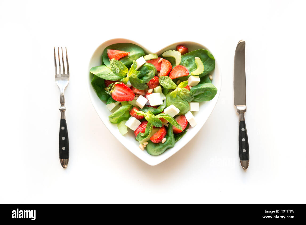 Insalata fresca di fragola, sedano, spinaci, pinoli, formaggio in piastra come cuore su bianco. Concetto di mangiare pulito per la disintossicazione. Vista da sopra. Foto Stock