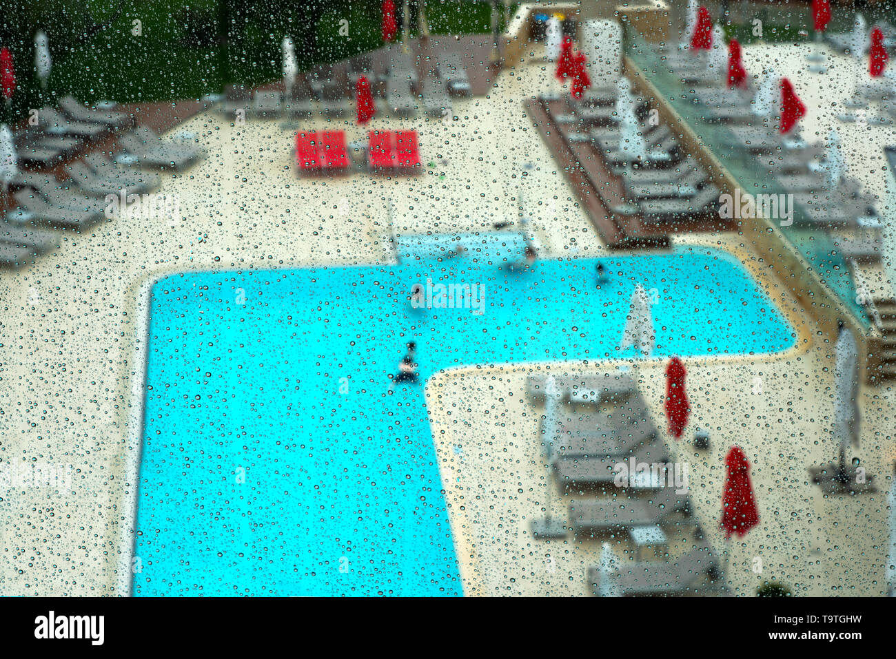 Vista attraverso una piovosa vetro per un paesaggio della piscina in estate Foto Stock