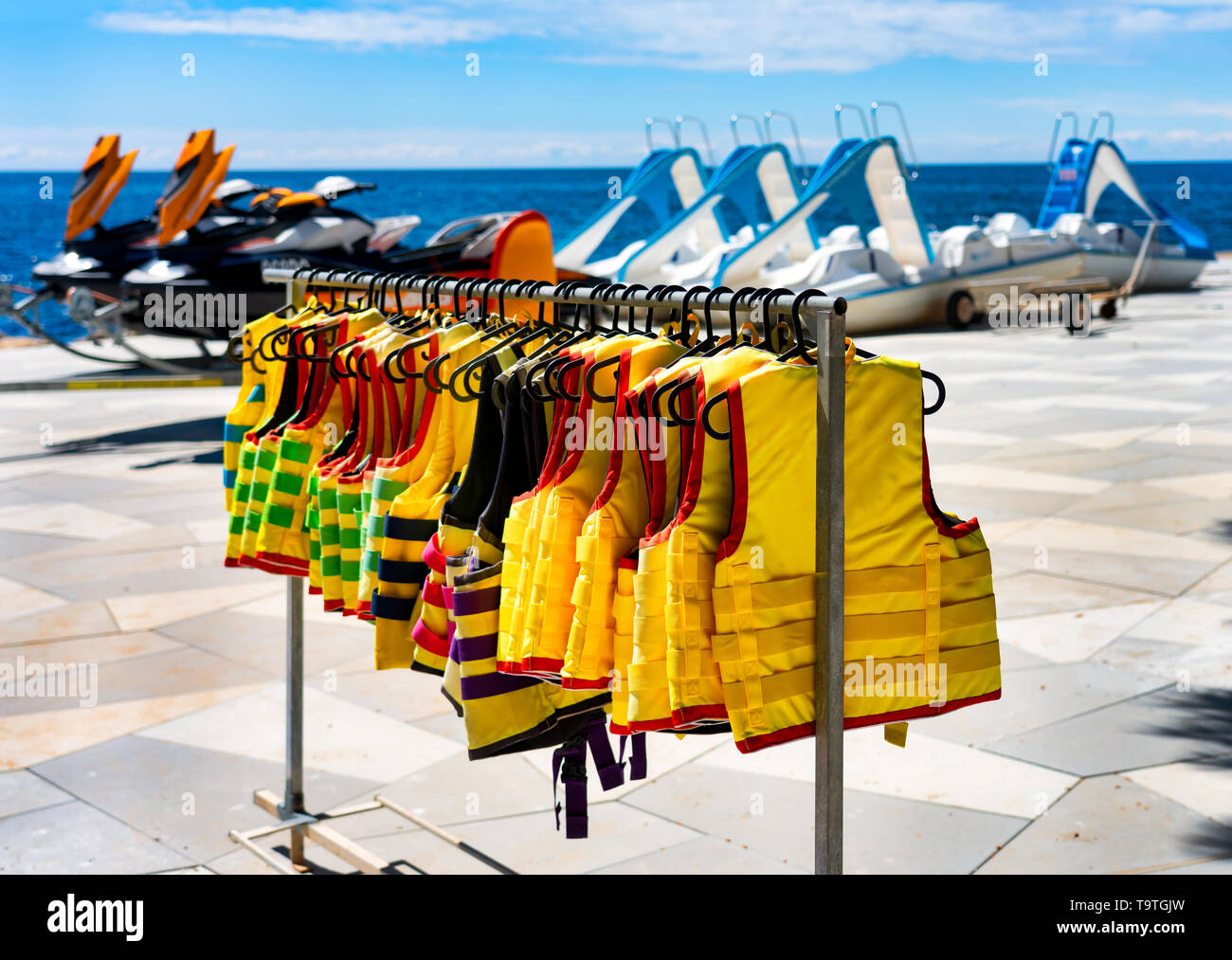 Un sacco di giubbotti di salvataggio appesa sulla spiaggia. Acqua scooter e barche a pedali in background. Il concetto di sicurezza dell'acqua. Foto Stock