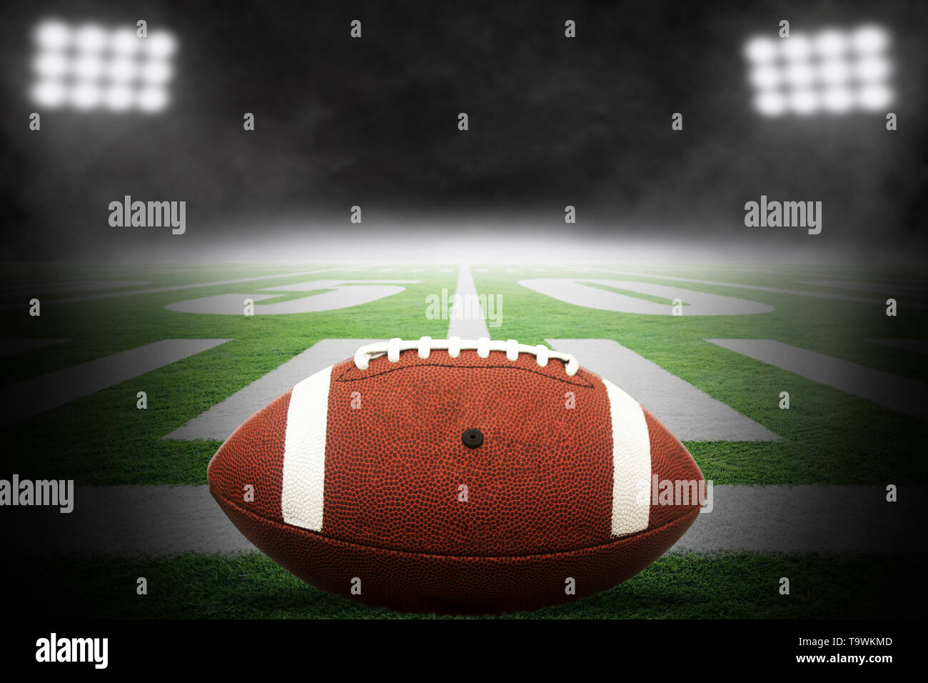 Close up del football americano sul campo dello stadio con linea di cantiere marcature e drammatica con Spotlight in salita sullo sfondo di nebbia e copia di spazio. Foto Stock