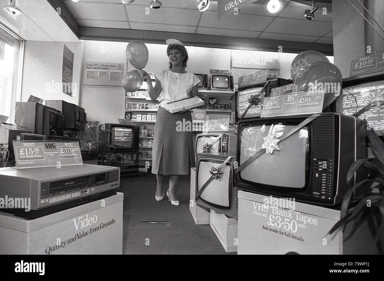 1985, storico, apparecchiature di home entertainment all'interno di un Granada Noleggio TV shop, una femmina shop assistant contiene una tastiera per un nuovo computer di casa insieme con alcuni ballons, Inghilterra, Regno Unito. Foto Stock