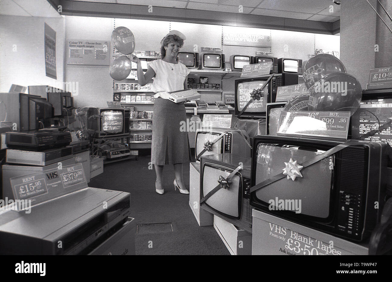 1985, storico, apparecchiature di home entertainment all'interno di un Granada Noleggio TV shop, una femmina shop assistant contiene un nuovo 'home computer insieme con alcuni ballons, Inghilterra, Regno Unito. Foto Stock