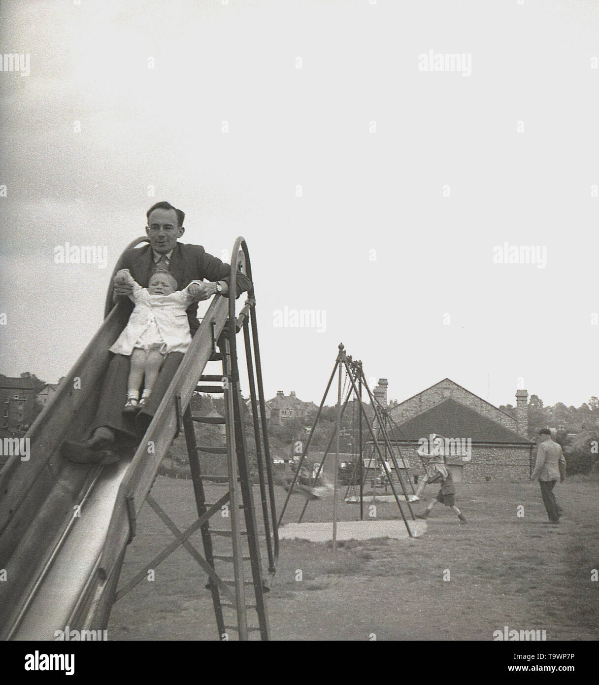Anni sessanta, storico, padre withhis neonato sulla parte superiore di un metallo slitta presso il locale parco giochi, Engalnd, UK. Foto Stock